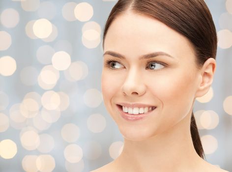 health, people and beauty concept - beautiful young woman face over holidays lights background