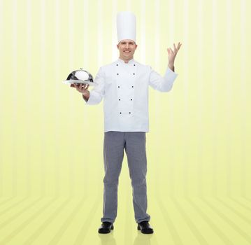 cooking, profession and people concept - happy male chef cook holding cloche over yellow background