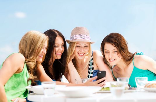 summer holidays, vacation and technology - girls looking at smartphone in cafe on the beach