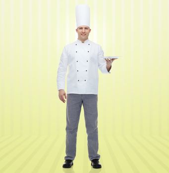 cooking, profession, advertisement and people concept - happy male chef cook showing something on empty plate over yellow background