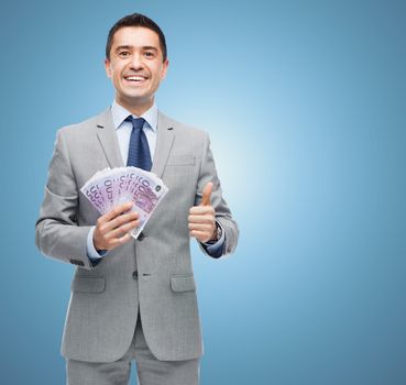 business, people and finances concept - smiling businessman with european money showing thumbs up over blue background