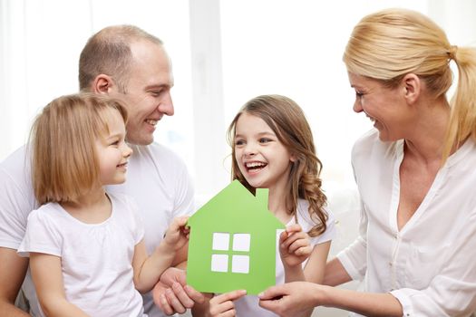 family, children, accommodation and home concept - smiling parents and two little girls at home with green house symbol