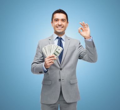 business, people and finances concept - smiling businessman with american dollar money over blue background
