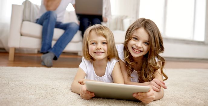 people, family, technology and children concept - happy little girls playing with tablet pc computer at home