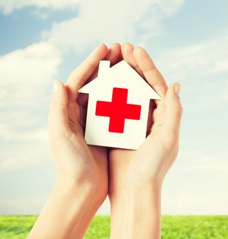 healthcare, medicine and charity concept - hands holding white paper house with red cross sign