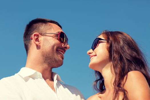 love, travel, tourism, people and friendship concept - smiling couple wearing sunglasses looking at each over blue sky background