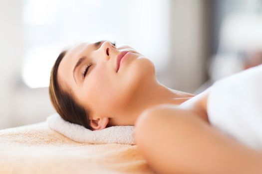 beauty and spa concept - beautiful woman in spa salon lying on the massage desk