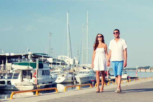 love, travel, tourism and people concept - smiling couple wearing sunglasses walking at harbor