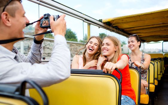 friendship, travel, vacation, summer and people concept - laughing friends with camera traveling by tour bus