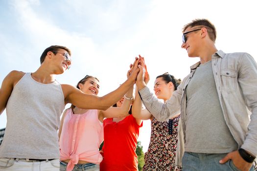 friendship, leisure, summer, gesturer and people concept - group of smiling friends making high five outdoors