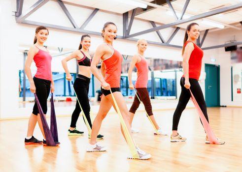 fitness, sport, training, gym and lifestyle concept - group of smiling people with instructor working out with rubber bands in the gym