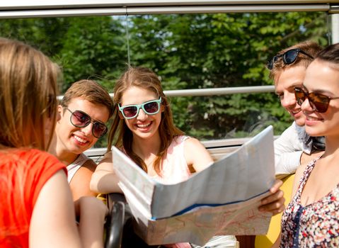 friendship, travel, vacation, summer and people concept - group of smiling friends with map traveling by tour bus