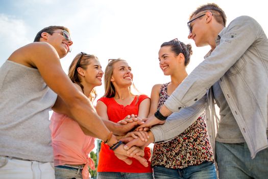 friendship, leisure, summer, gesturer and people concept - group of smiling friends with hands on top in city