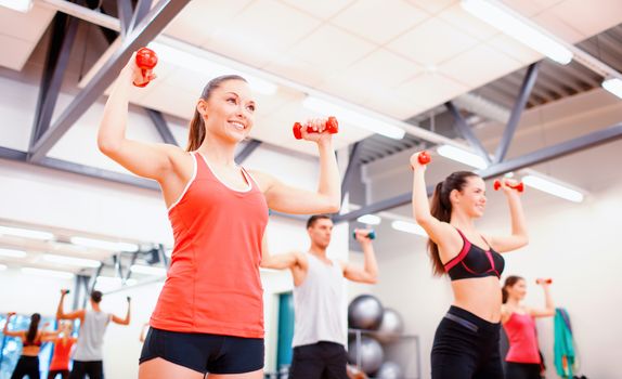 fitness, sport, training, gym and lifestyle concept - group of smiling people working out with dumbbells in the gym