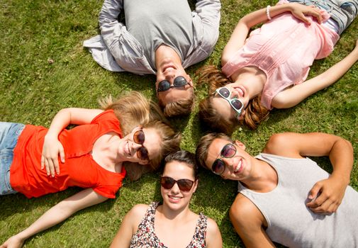friendship, leisure, summer and people concept - group of smiling friends lying on grass in circle outdoors