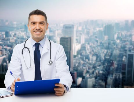 medicine, profession, technology and people concept - happy male doctor with clipboard and stethoscope over city background