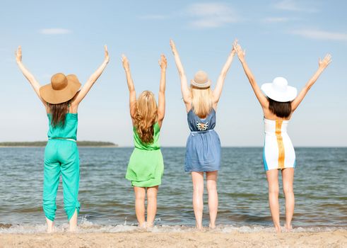 summer holidays and vacation concept - girls with hands up on the beach