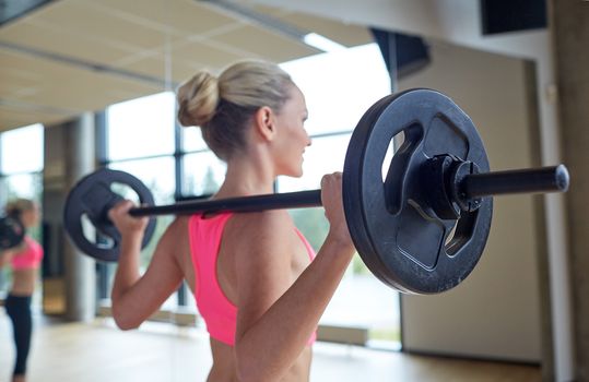 fitness, sport, training, people and lifestyle concept - happy woman flexing muscles with barbell in gym