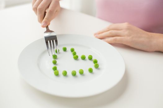healthy eating, dieting, vegetarian food and people concept - close up of woman with fork eating peas in shape of heart