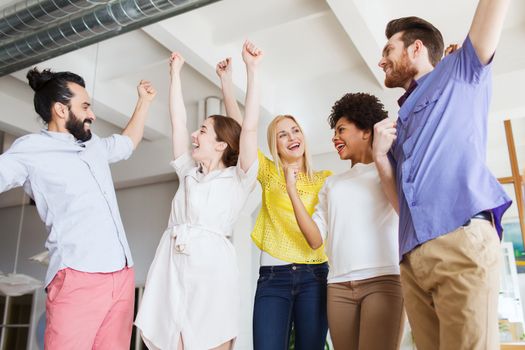 business, triumph, gesture, people and teamwork concept - happy creative team raising hands up and celebrating victory in office