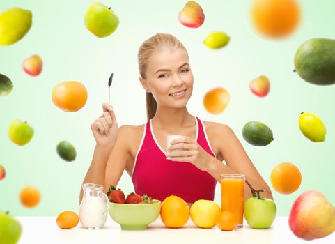 healthy eating, diet, organic food and people concept - happy woman eating yogurt and having breakfast over green background with falling fruits