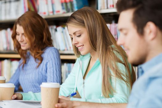 people, knowledge, education and school concept - group of happy students reading books, drinking coffee and preparing to exam in library