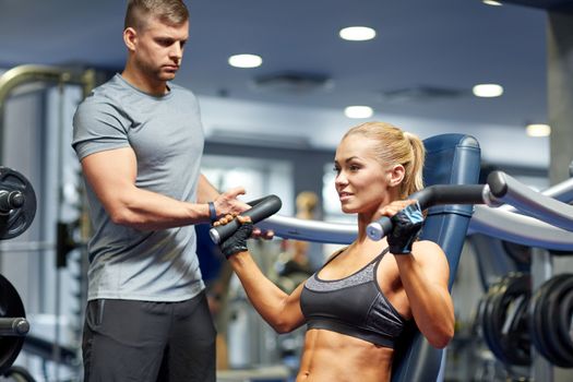 sport, fitness, bodybuilding, teamwork and people concept - young woman and personal trainer flexing muscles on gym machine