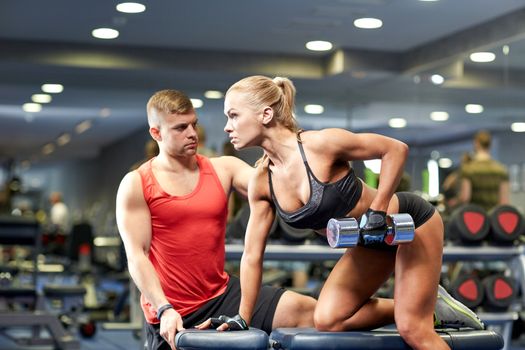 fitness, sport, exercising, bodybuilding and weightlifting concept - young woman and personal trainer with dumbbells flexing muscles in gym