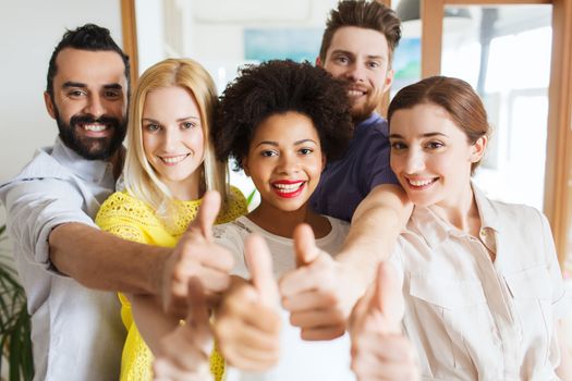 business, startup, people and teamwork concept - happy creative team showing thumbs up in office