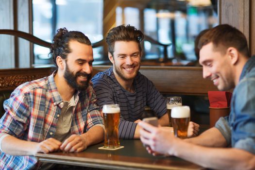 people, men, leisure, friendship and technology concept - happy male friends with smartphone drinking beer at bar or pub