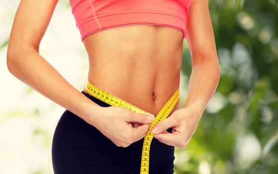 diet, sport, fitness and heath concept - close up of female hands measuring waist with measuring tape