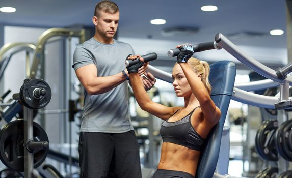 sport, fitness, bodybuilding, teamwork and people concept - young woman and personal trainer flexing muscles on gym machine