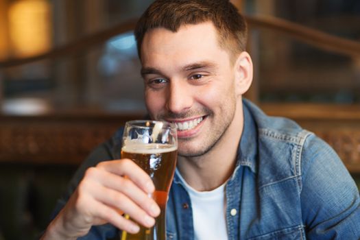 people, drinks, alcohol and leisure concept - happy young man drinking beer at bar or pub