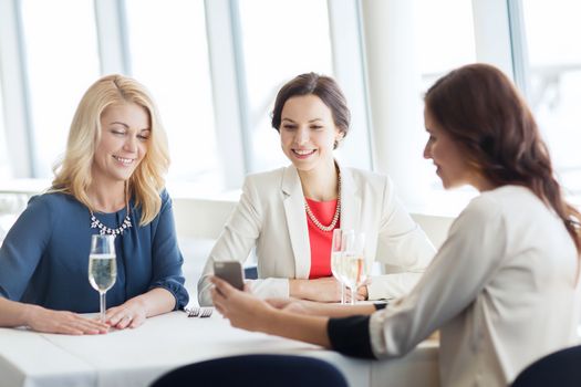 people, holidays, technology and lifestyle concept - happy women with smartphone drinking champagne at restaurant