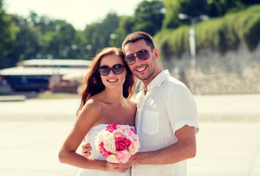 love, wedding, summer, dating and people concept - smiling couple wearing sunglasses with bunch of flowers hugging in city