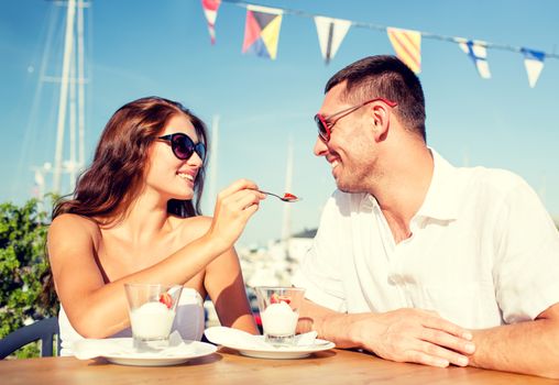 love, dating, people and food concept - smiling couple wearing sunglasses eating dessert and looking to each other at cafe