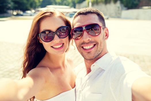 love, wedding, summer, dating and people concept - smiling couple wearing sunglasses making selfie in city