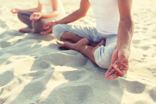 fitness, sport, people and lifestyle concept - close up of couple making yoga exercises sitting on pier outdoors