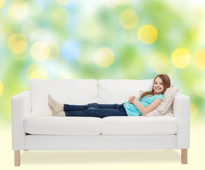 home, leisure, people and happiness concept - smiling little girl lying on sofa over green lights background