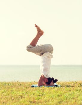 fitness, sport, people and lifestyle concept - man making yoga exercises on sand outdoors