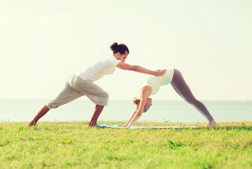 fitness, sport, friendship and lifestyle concept - smiling couple making yoga exercises on mat outdoors