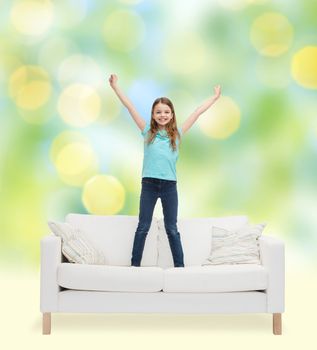 home, leisure, people and happiness concept - smiling little girl jumping on sofa over green lights background