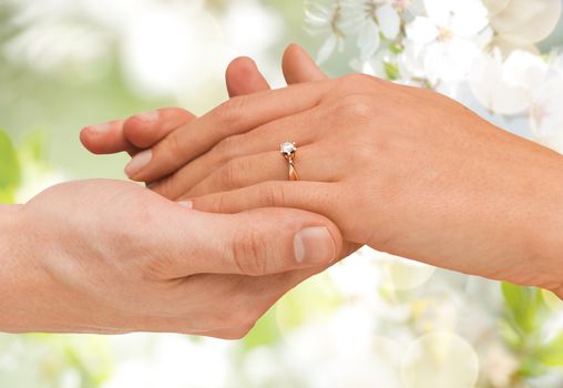 jewelry, couple, love and wedding concept - close up of man and woman hands with engagement ring over summer garden and cherry blossom background