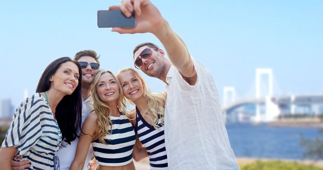 summer, tourism, asia, technology and people concept - group of smiling friends taking selfie with smartphone over rainbow bridge in japan background