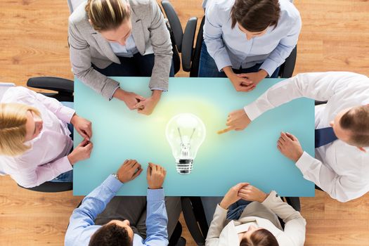 business, people and team work concept - close up of creative team sitting at table and pointing finger to lighting bulb in office