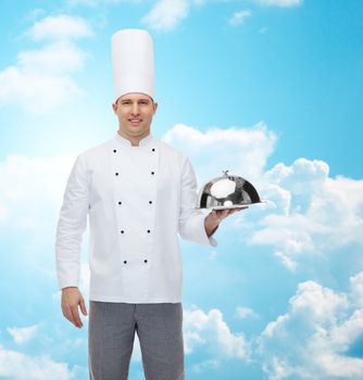 cooking, profession and people concept - happy male chef cook holding cloche over blue sky with clouds background