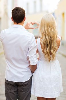 summer holidays, love, travel, tourism, relationship and dating concept - romantic couple in the city making heart shape