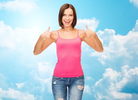 people, advertisement and clothing concept - smiling woman in blank pink tank top pointing fingers to herself over blue sky with white clouds background