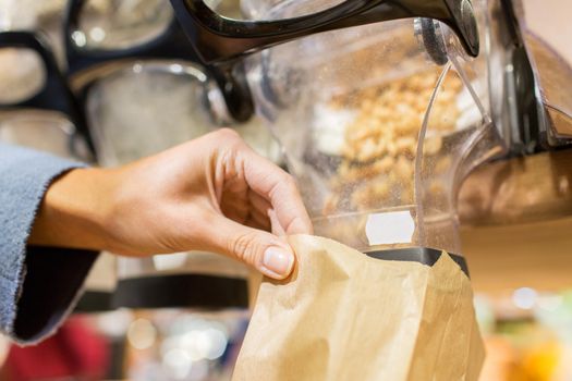 sale, shopping and eco food concept - close up of female hand pouring nuts to paper bag at grocery store