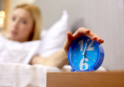 morning, awakening and people concept - close up of female hand on alarm clock in bedroom